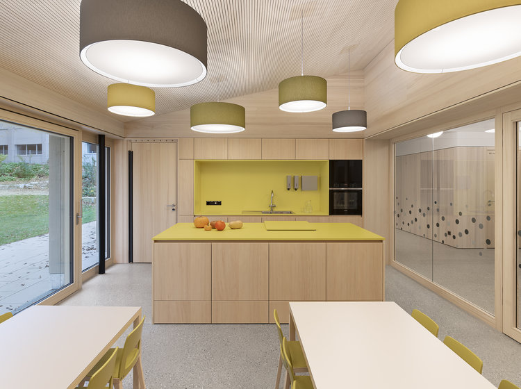 Moderne Küche mit Essbereich Moderne Küche mit gelber Rückwand, Kochinsel und großen Hängelampen; angrenzender Essbereich mit weißen Tischen und grün-gelben Stühlen.