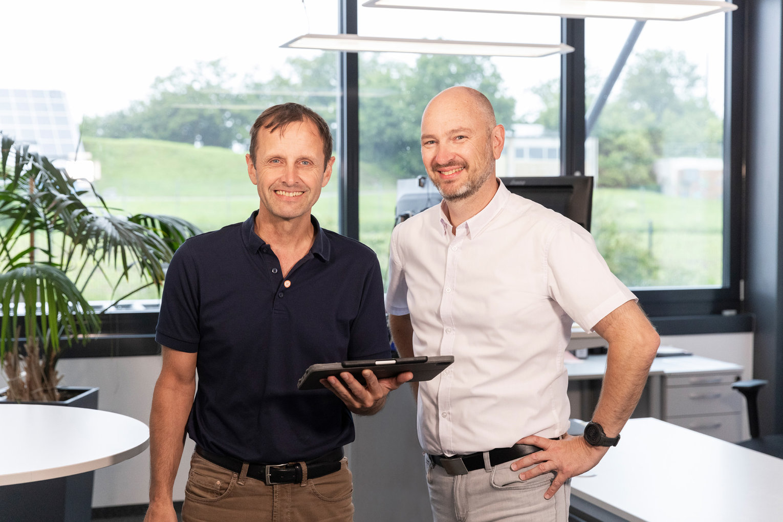 Zwei Männer stehen nebeneinander im Büro, einer hält ein Tablet